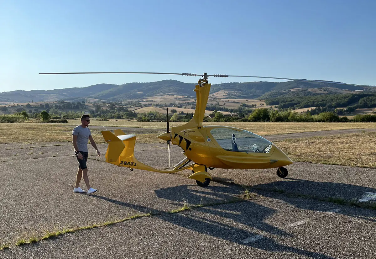 Vincent Desfond marche près de l'autogire jaune sur l'aérodrome, collines en arrière-plan
